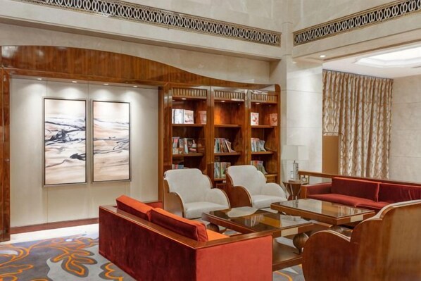 A hotel lobby with a curved wooden wall, a seating area with a red sofa and white chairs, a coffee table, and a bookshelf.