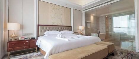 A hotel room with a large bed, a bedside table, a bench, a large mirror, and a view of the city.