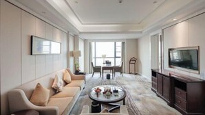 A spacious living room with a sofa, coffee table, TV, and a dining area. - Fairyland International Hotel (Xiantao)