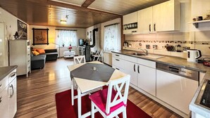 Una cocina compacta con armarios blancos, una mesa de comedor con sillas y una alfombra roja.