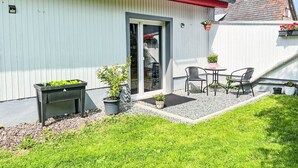Eine Terrasse mit Tisch und Stühlen, ein kleiner Gartenbereich mit Topfpflanzen und ein Gebäude mit rotem Dach und weißen Wänden.