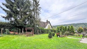 Un jardín bien cuidado con un columpio de madera, una casa blanca con techo de tejas y una variedad de plantas y árboles.