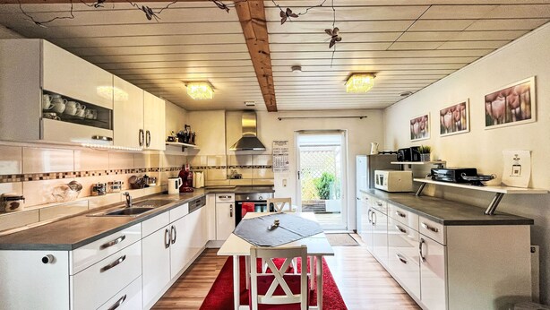 Una cocina moderna con armarios blancos, un tapete rojo y un techo de madera.