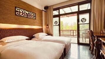 A hotel room with two beds, a wooden headboard, a dining table, and a large glass door leading to an outdoor area.