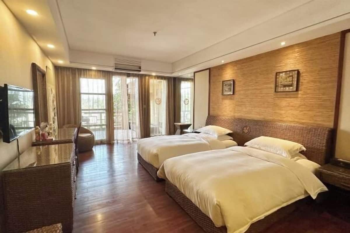 A hotel room with two beds, a TV, a desk, and a large window.