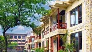 A row of traditional-style buildings with stone facades, wooden balconies, and a calm water body in the foreground. - Tianci Hot Spring Resort (Chongqing)
