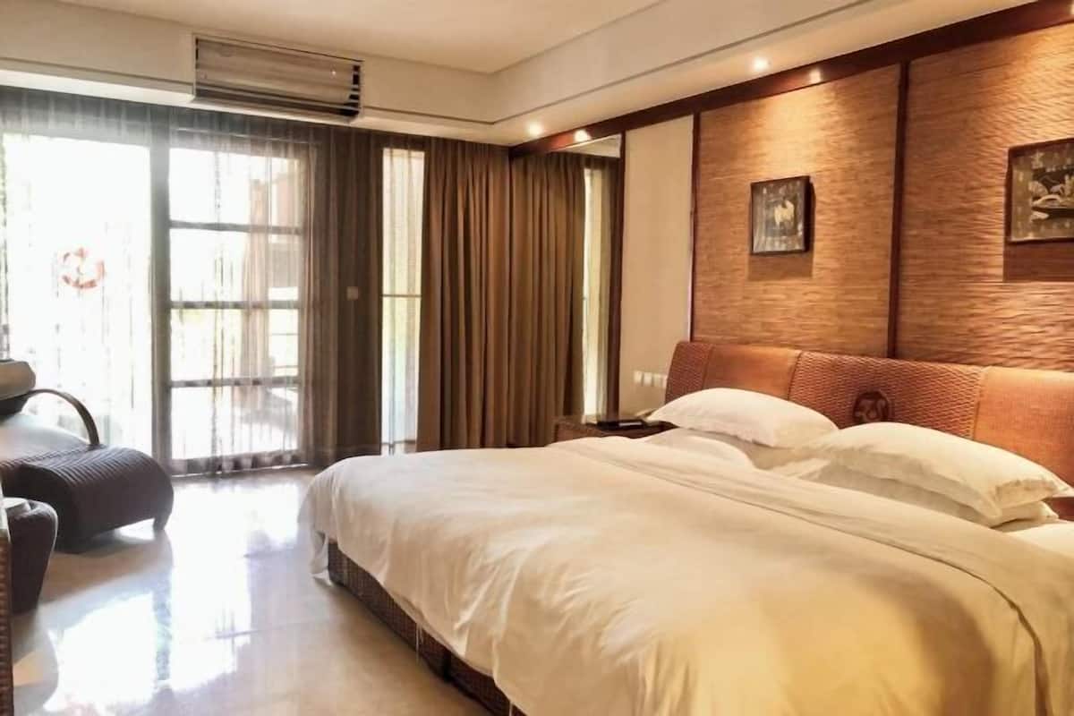 A hotel room with a large bed, a seating area with a chair, and a view of the outdoors through a large window.