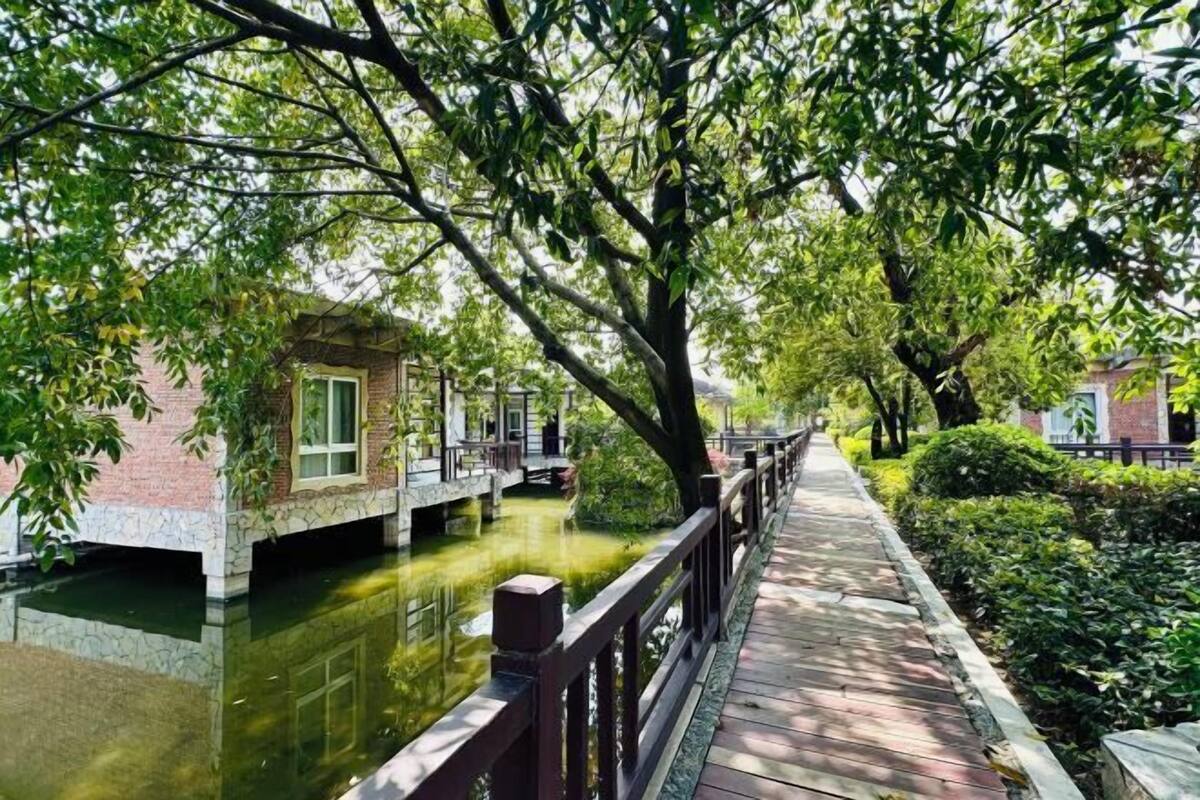 A wooden bridge over a calm water body, surrounded by lush greenery and traditional buildings.