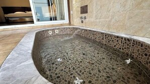 A stone-tiled hot tub with a glass door leading to a bedroom. - Tianci Hot Spring Resort (Chongqing)