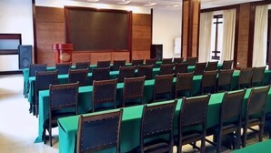 A conference room with rows of tables and chairs, a podium, and a large screen. - Tianci Hot Spring Resort (Chongqing)
