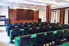 Una sala conferenze con file di tavoli e sedie, un podio e un grande schermo.