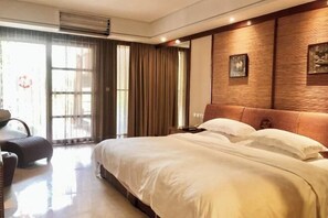 Ein Hotelzimmer mit einem großen Bett, einer Sitzecke mit einem Sessel, einem Holz-Kopfteil und einem großen Fenster mit Vorhängen.