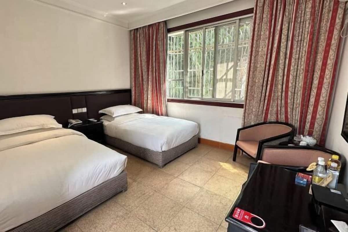 A hotel room with two single beds, a desk with a chair, and a window with curtains.