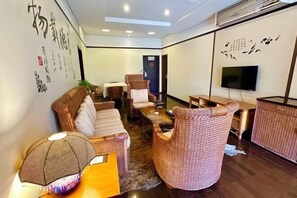 Ein modernes Wohnzimmer mit Rattanmöbeln, einem Flachbildfernseher und dekorativen Wandbildern.