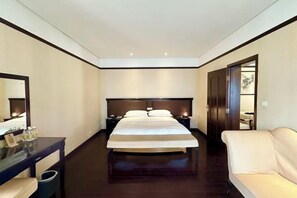 Ein Hotelzimmer mit einem großen Bett, Nachttischen, einem Spiegel, einem Sofa und einer Tür zu einem anderen Raum.