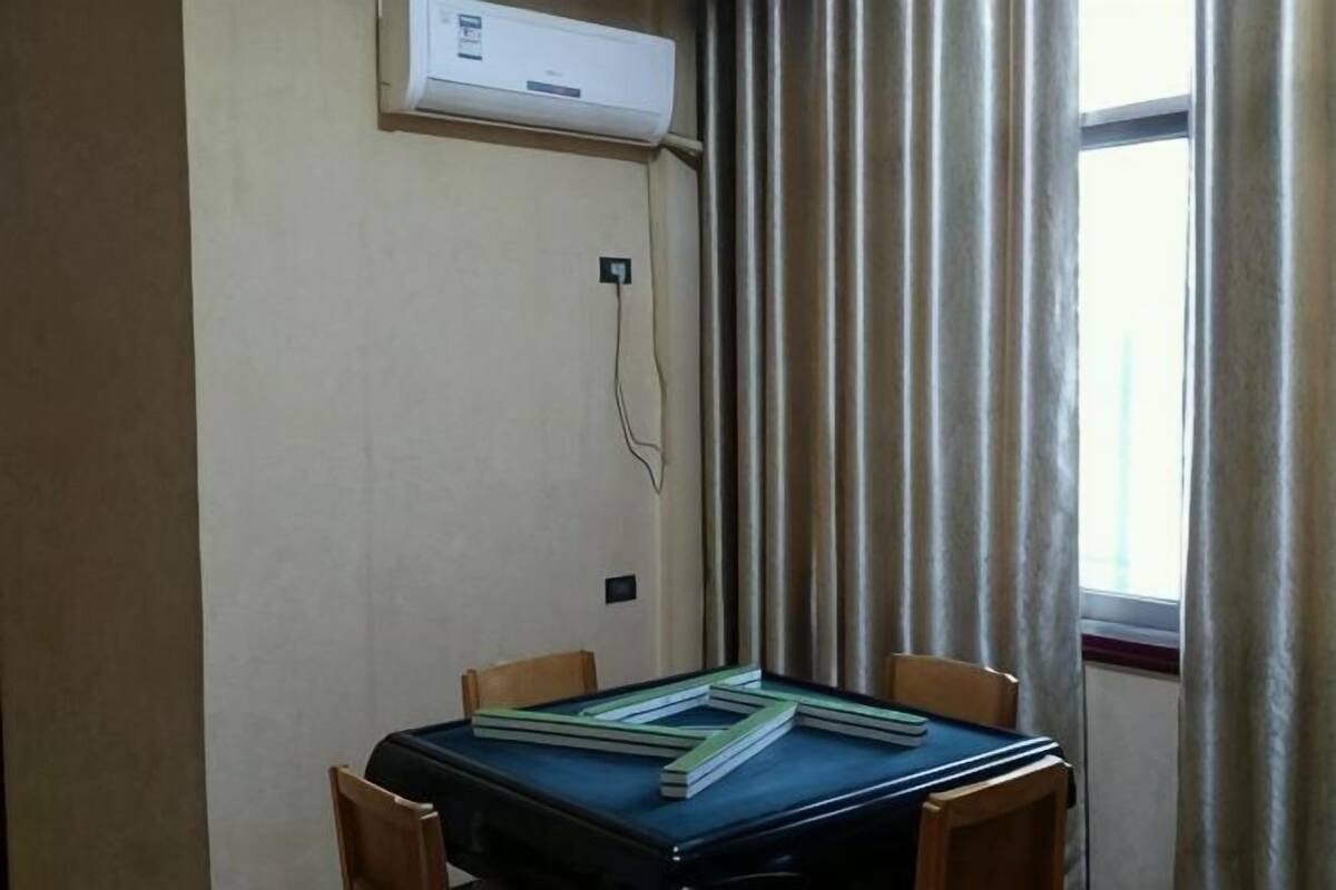 Een kamer met een tafel, stoelen, een airconditioning, een raam met gordijnen en een stopcontact.
