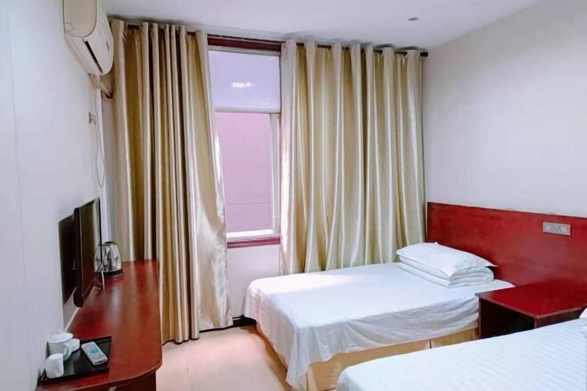 Een hotelkamer met twee eenpersoonsbedden, een televisie, een koffiezetapparaat en een raam met gordijnen.