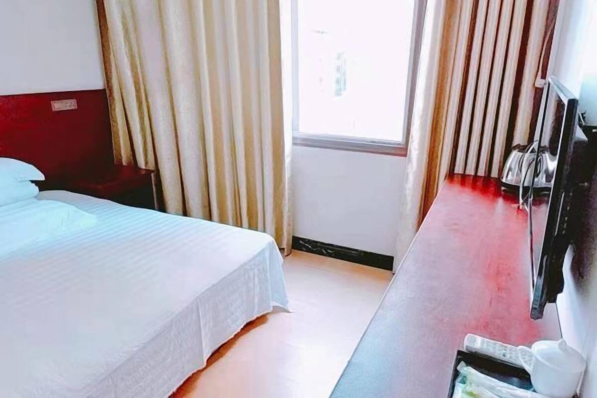 Een hotelkamer met een bed, bureau, stoel en raam met gordijnen.