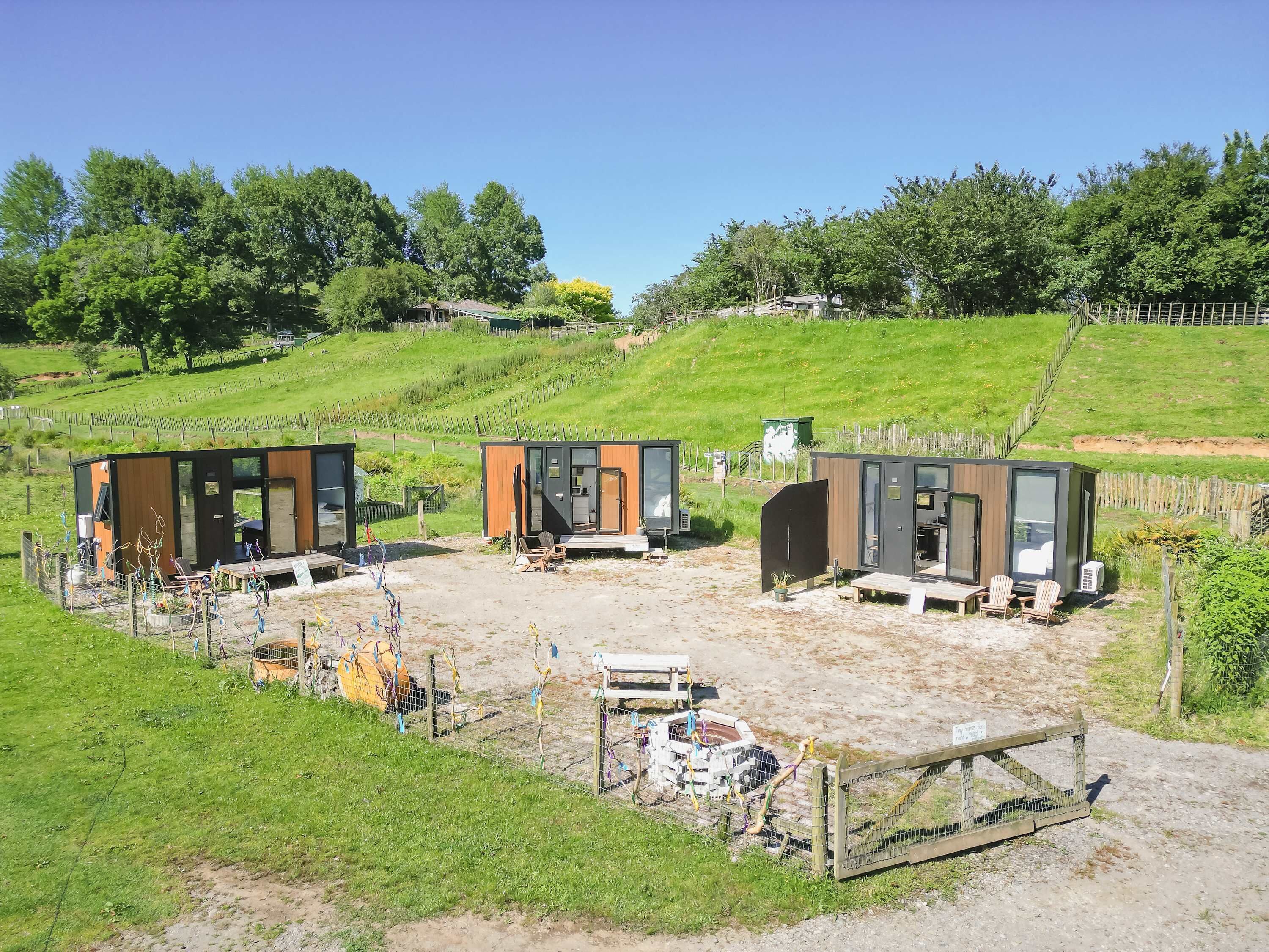 Tres cabañas modernas y compactas con ventanas amplias, ubicadas en una colina cubierta de hierba bajo un cielo despejado.