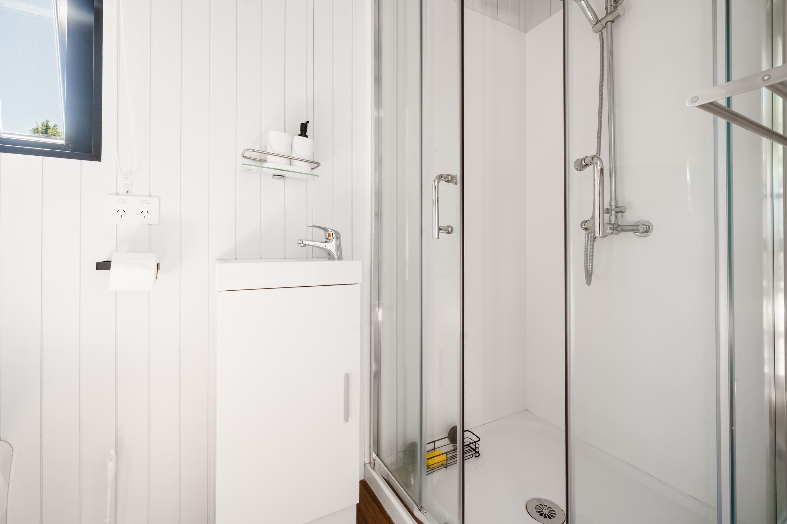 A modern bathroom with a glass-enclosed shower, a white sink, and a shelf with toiletries.