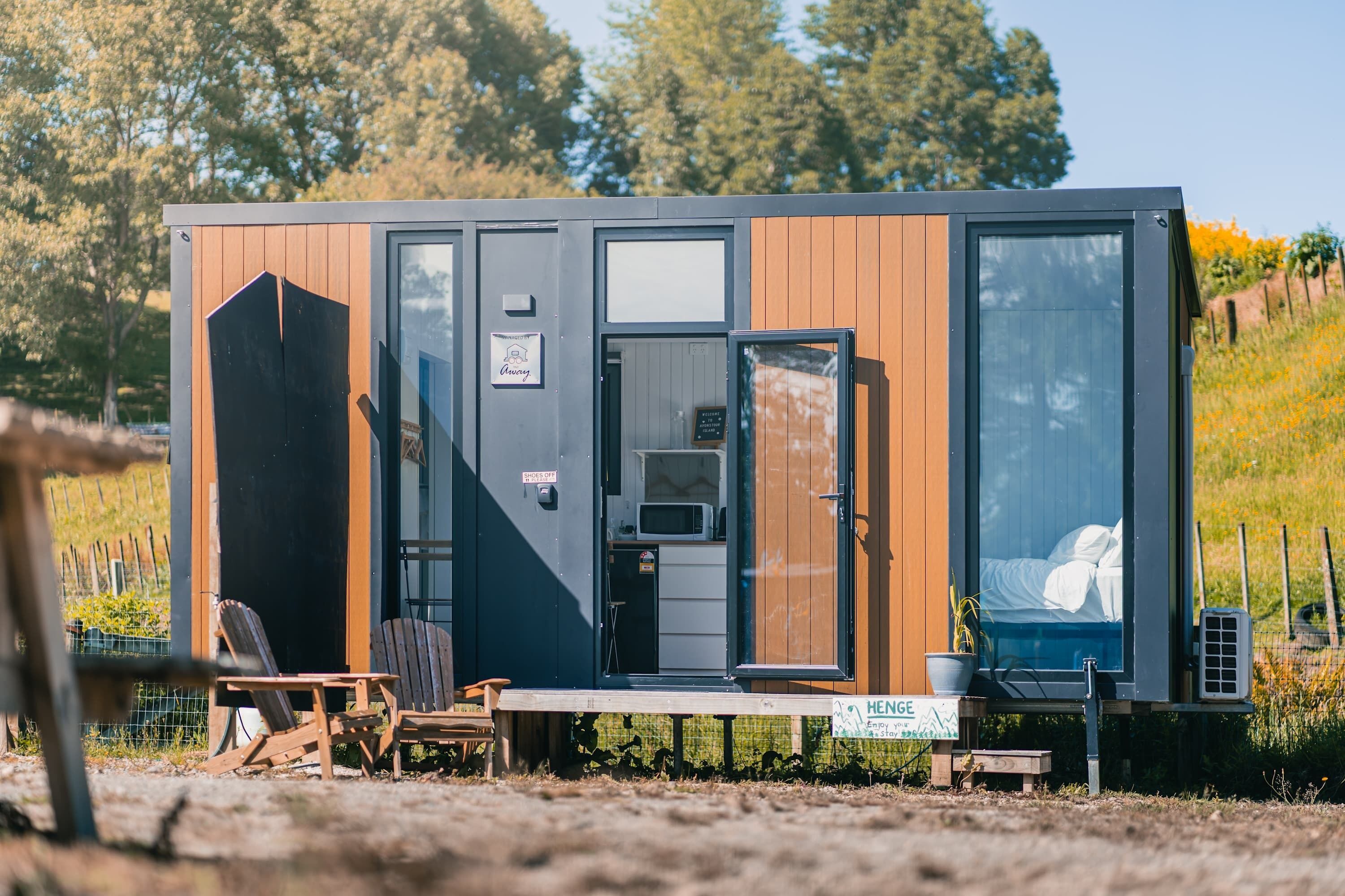 Una cabaña moderna y compacta con fachada de madera, una kitchenette pequeña y una cama individual.