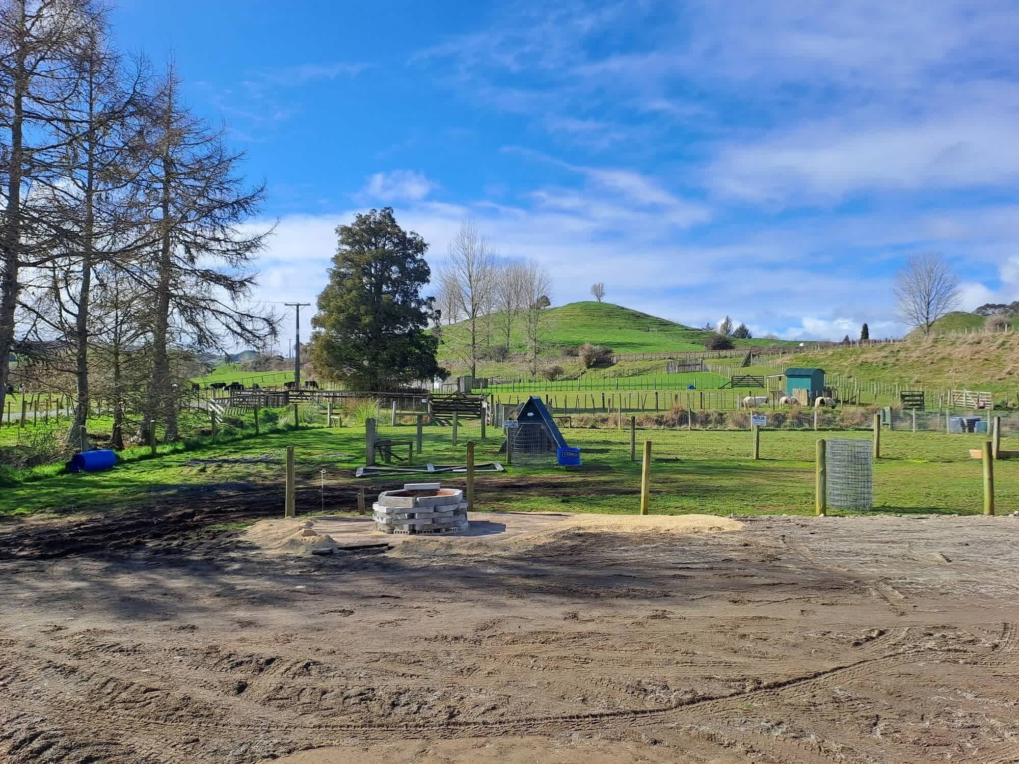 A rural landscape with a fenced area, a small building, and a hill in the background.