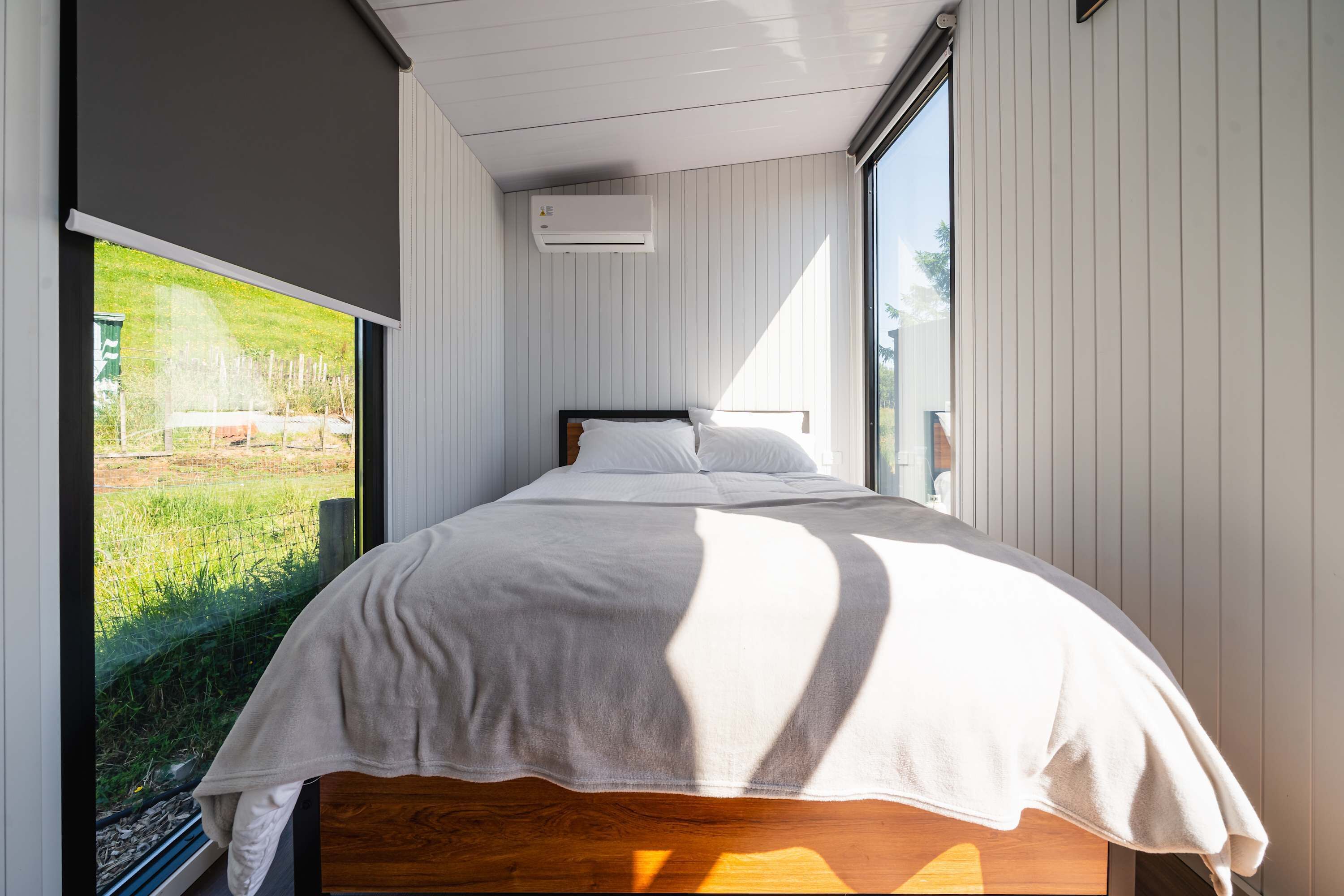 Un dormitorio con un ventanal grande, una cama con ropa de cama blanca y un cabecero de madera.