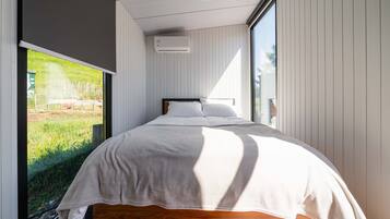 A bedroom with a large window, a bed with white bedding, and a wooden headboard.