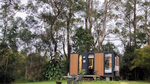A modern, compact cabin with a wooden exterior and a glass door, situated in a lush, green forest.