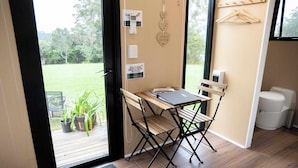 A compact room with a wooden desk, a chair, and a small table. There is a door leading to an outdoor area with potted plants.