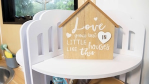 A wooden house-shaped sign with the text "Love grows best in little houses like this" on a white chair.