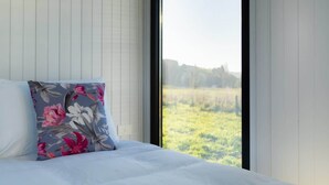 A bedroom with a bed, a floral pillow, and a window with a view of a field.
