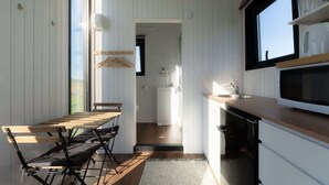A compact kitchen with a wooden table and chairs, a microwave, and a window overlooking a garden.