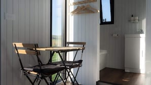 A compact room with a dining table and chairs, a small kitchenette, and a window with a wooden hanger rack.