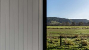 Vista a través de una ventana de un paisaje rural con campos y colinas.