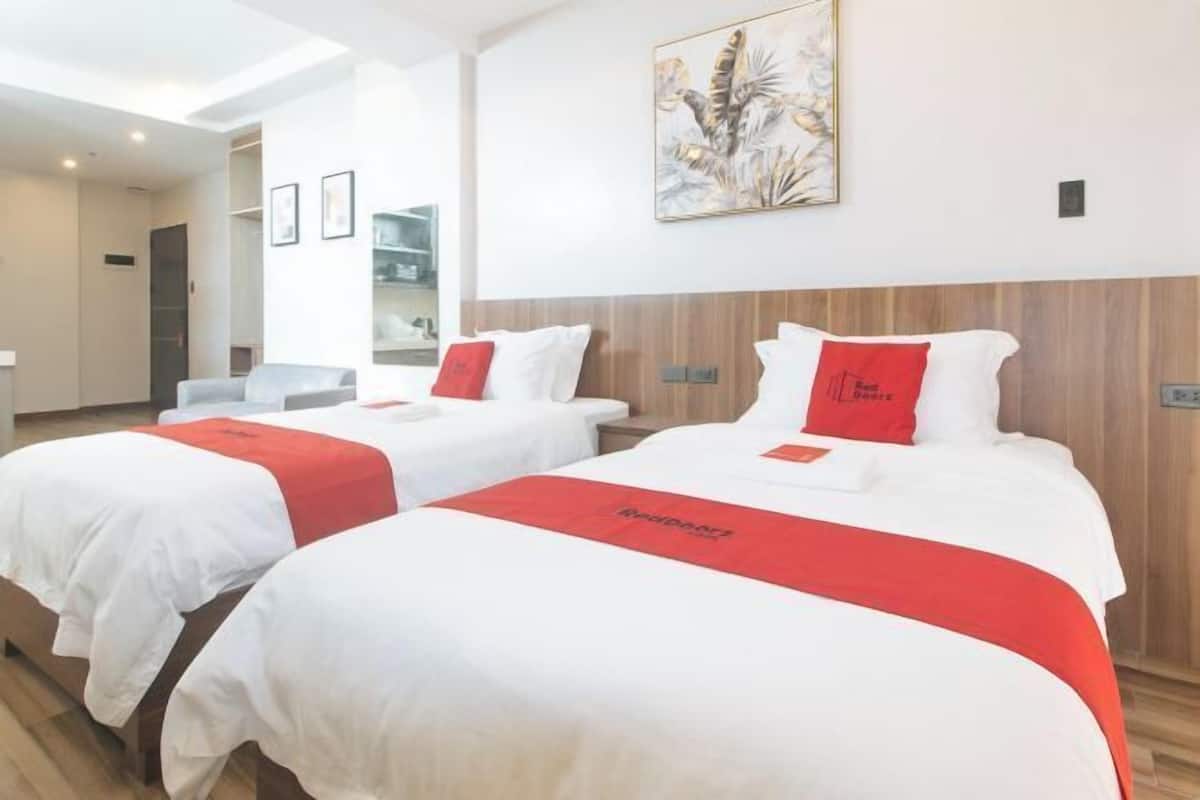 Une chambre d’hôtel avec deux lits, chacun recouvert d’une couvre-lit rouge et blanche, doté d’une tête de lit en bois et orné d’une œuvre d’art accrochée au mur.