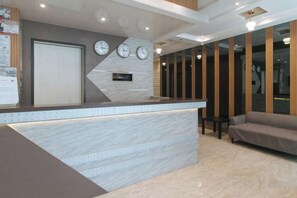 A reception area with a marble counter, clocks, a sofa, and a wooden panel wall.