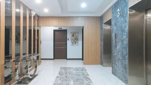 A modern lobby with a marble floor, wooden paneling, a glass reception desk, and an elevator. - RedDoorz Plus @ Bez Tower and Residences San Juan (San Juan)