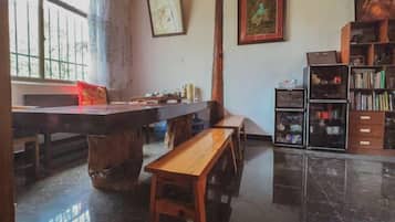 Een kamer met een eettafel, bankjes, een boekenkast en een raam met gordijnen.