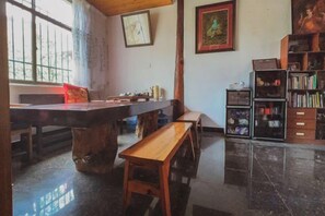 Una habitación con una mesa de comedor, bancos, una estantería y una ventana con cortinas.