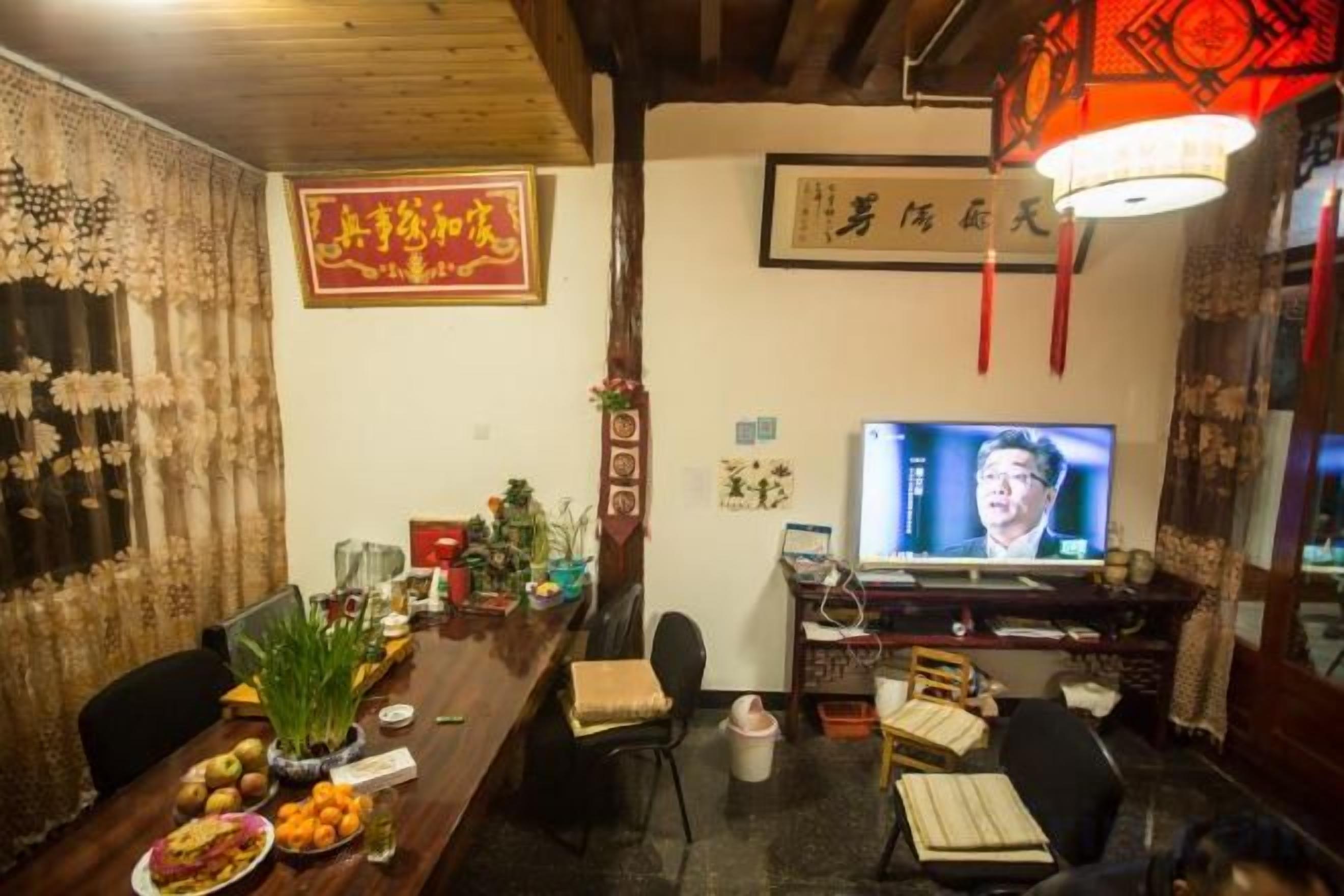 A traditional room with a wooden ceiling, a television, a desk with a computer, and a dining table with fruits and a vase.