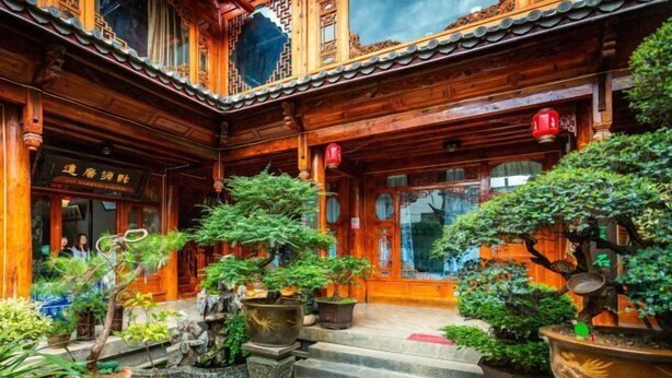 A traditional wooden building with a tiled roof, a staircase leading to the entrance, and various potted plants. - Songhe Boutique Hostel (Lijiang)