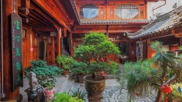 A traditional courtyard with wooden architecture, potted plants, and a tiled floor.