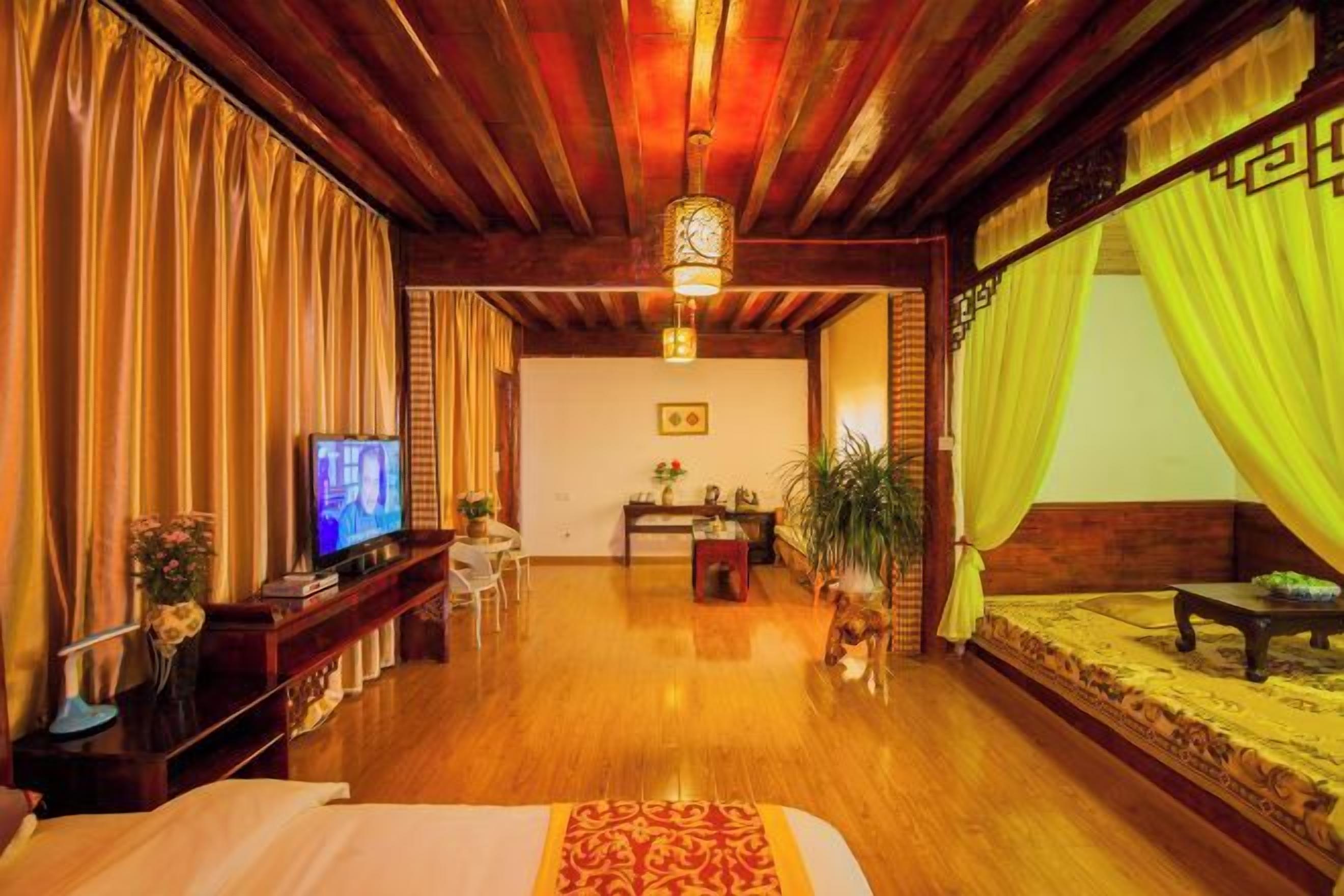 A hotel room with a wooden ceiling, a bed with a patterned bedspread, a television, a desk with a chair, and a sofa with a patterned rug.