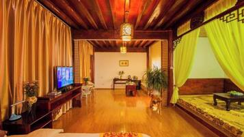 A hotel room with a wooden ceiling, a bed with a patterned bedspread, a television, a desk with a chair, and a sofa with a patterned rug.