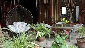 A hanging chair with a floral cushion, a table with chairs, and various potted plants.