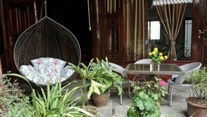 A hanging chair, a table with chairs, and potted plants in a courtyard. - Songhe Boutique Hostel (Lijiang)