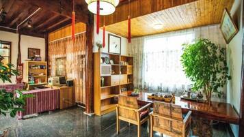 A traditional interior with a wooden ceiling, a desk with a chair, a bookshelf, and a large plant.