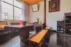 Un comedor con mesa de madera, bancos y refrigerador.