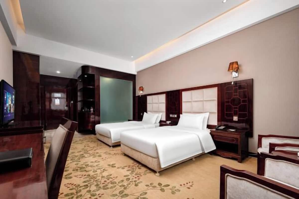 A hotel room with two beds, a desk, a chair, and a TV.